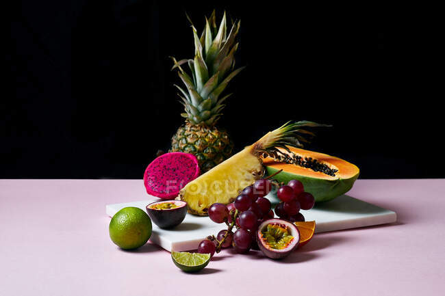 Natureza morta com frutas tropicais: mamão fatiado, abacaxi, pitaia e uvas na tábua de corte de mármore — Fotografia de Stock