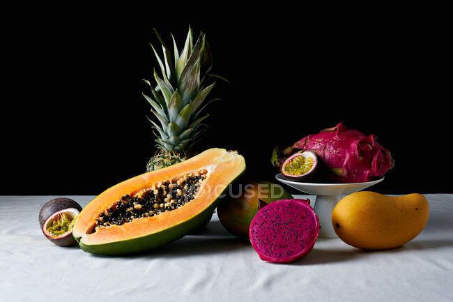 Stillleben mit tropischen Früchten auf weißer Tischdecke und dunklem Hintergrund — Stockfoto