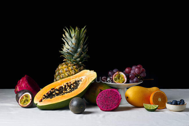 Natureza morta com frutas tropicais na toalha de mesa branca e fundo escuro — Fotografia de Stock