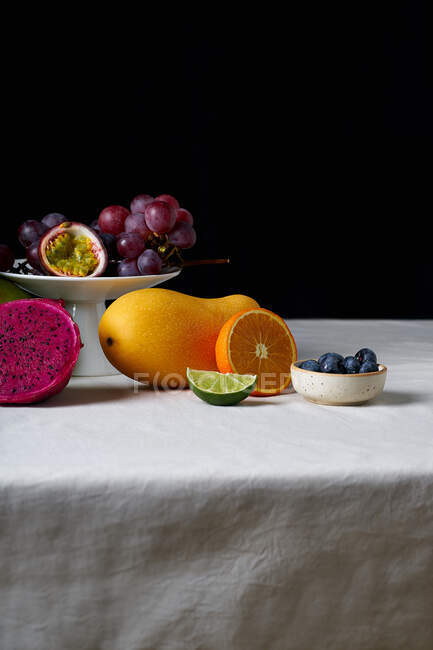 Still life with tropical fruits on white tablecloth and dark background — Stock Photo