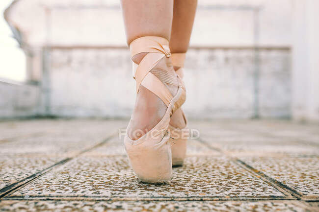 Crop female dancer wearing pointe shoes standing on tiptoes on weathered stone ground and demonstrating dancing position — Stock Photo