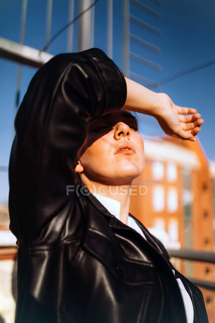 Heitere Frau in trendiger Lederjacke steht mit geschlossenen Augen auf Sommerterrasse und genießt sonniges Wetter — Stockfoto
