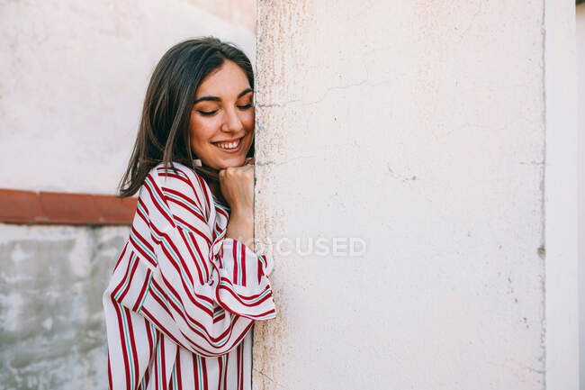 Side view of tranquil female wearing stylish clothes leaning on shabby stone wall on street with closed eyes — Stock Photo