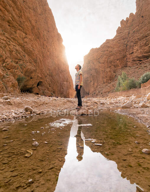 Низький кут зору чоловічого туриста в повсякденному одязі, що стоїть на камені у воді і захоплюється дивовижним видом на грубі скелі — стокове фото