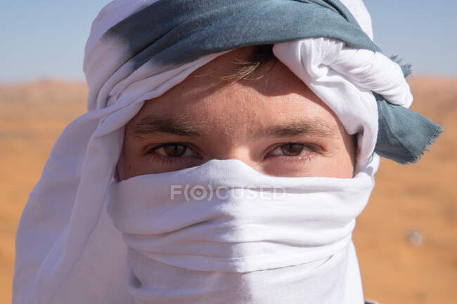 Crop portrait of young male tourist covering face and mouth from sand during vacation in desert Morocco and looking at camera — Stock Photo