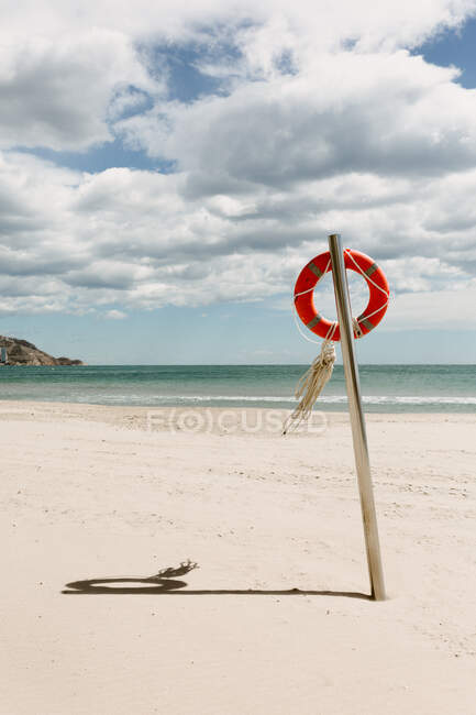 Seascape of empty coastline with lifesaver placed on metal pole on background of cloudy sky — Stock Photo
