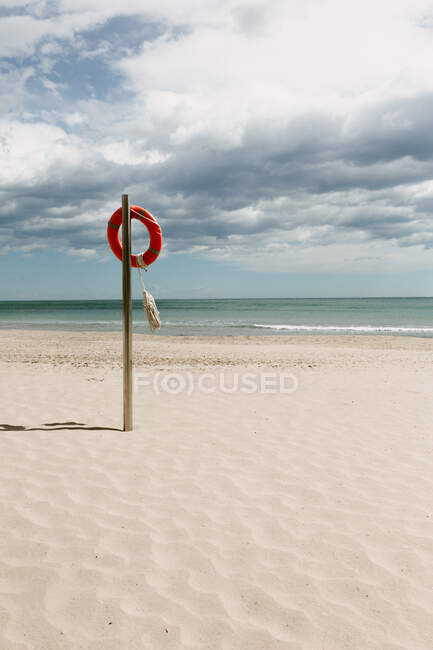 Seascape of empty coastline with lifesaver placed on metal pole on background of cloudy sky — Stock Photo