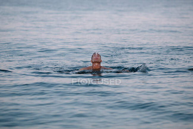 Nadador masculino satisfecho durante el ocio activo saludable en aguas profundas tranquilas mientras escupe agua después de bucear en el día soleado durante las vacaciones - foto de stock