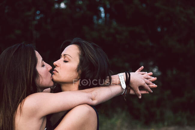 Ніжні коханки-жінки в повсякденному вбранні цілуються один з одним закритими очима під час виходу на вулицю на розмитому фоні в сонячний літній день — стокове фото