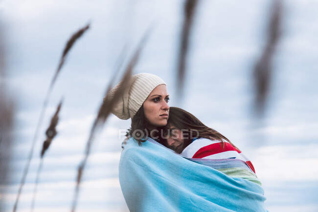 Бічний вид на жінок, які обгортають прапор Великої Британії, обіймаючись, дивлячись на морське узбережжя і хмарне небо під час романтичних вихідних — стокове фото