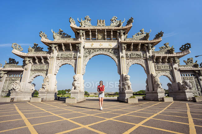 Von unten einer schlanken Reisenden, die ein Foto mit einer Fotokamera macht, während sie auf dem Bürgersteig in der Nähe der Fassade des chinesischen Tempels steht, mit Bögen, die mit Skulpturen dekoriert sind — Stockfoto