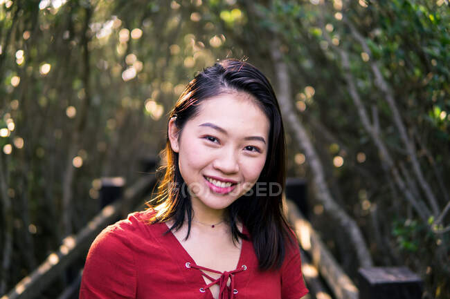 Thoughtful young Asian female in casual wear and small necklace looking at camera while standing in forest in daylight — Stock Photo