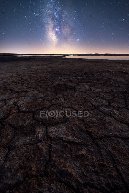Dry cracked surface of ground and colorful night starry sky on horizon — Stock Photo