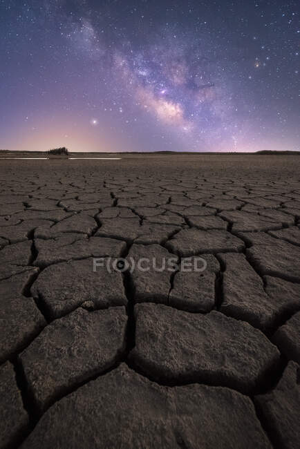 Dry cracked surface of ground and colorful night starry sky on horizon — Stock Photo