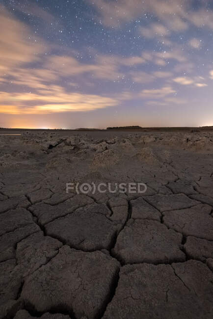 Siccità incrinato terreno privo di vita sotto cielo nuvoloso colorato al tramonto — Foto stock