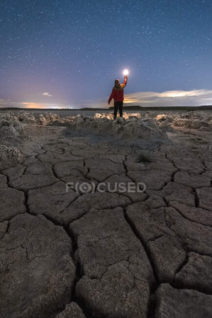 Silhouette di uomo irriconoscibile in piedi con torcia in mano su maestoso scenario di terreno vulcanico con rocce porose e colorato Via Lattea su sfondo — Foto stock