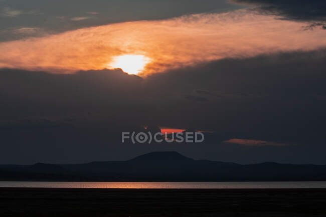Silhouette della catena montuosa e sorprendente tramonto riflesso in acque tranquille del lago — Foto stock