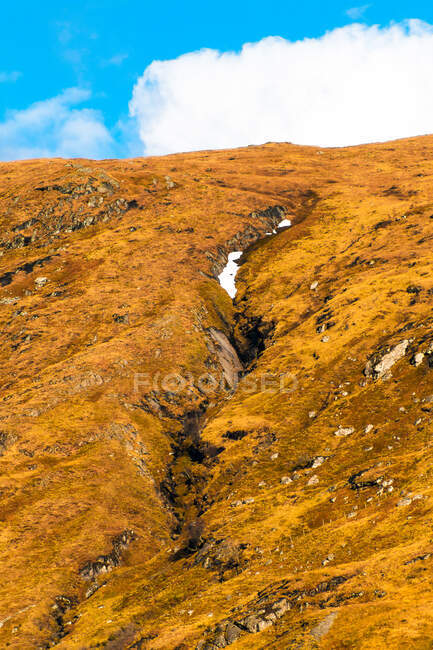 Живописный вид горного склона покрытого снегом среди зеленых холмов с лесом против облачного неба в весенний день в Шотландском нагорье — стоковое фото