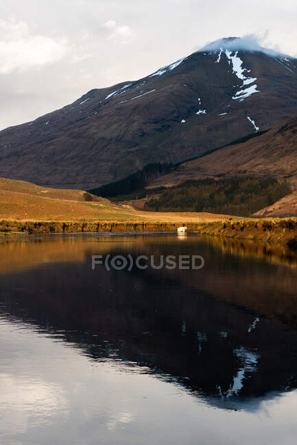 Malerische Landschaft mit Kühen, die an einem sonnigen Frühlingstag im schottischen Hochland auf grünem Gras in der Nähe des ruhigen Flusses gegen den Berg weiden — Stockfoto