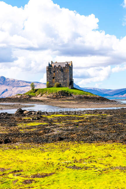 Яскравий весняний пейзаж з середньовічним кам'яним замком, розташований на пагорбі біля річки в зеленій долині в Шотландському нагір'ї в сонячний день з хмарним небом. — стокове фото