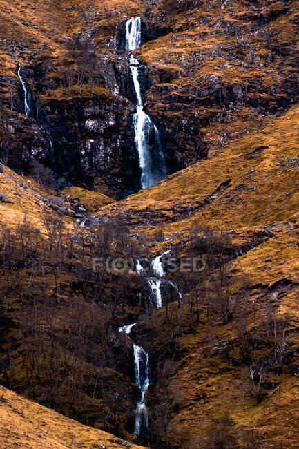 Rough rocky mountain slope with leafless bushes and waterfall in Scottish Highlands — Stock Photo