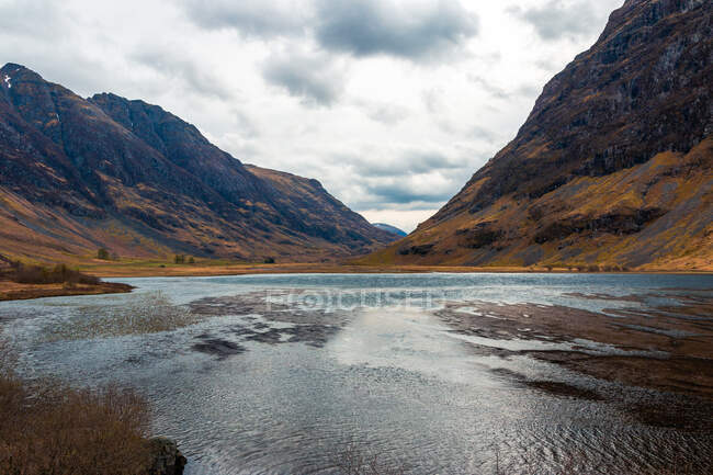 Amazing Scottish landscape of calm lake with mirrored surface reflecting mountain with snow covered peak and blue cloudy sky in Glen Coe area — Stock Photo