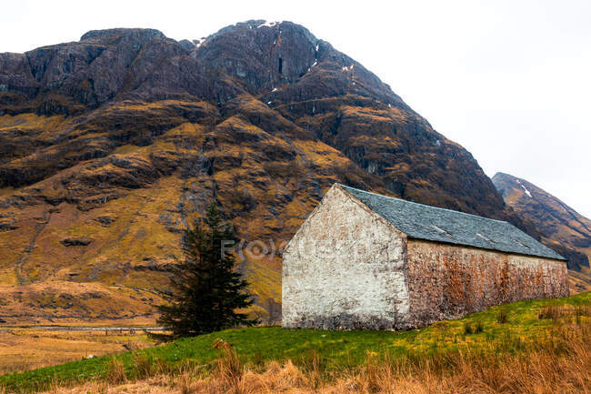 Altes Steinhaus auf grünem Hügel gegen majestätischen Felsenberg in den schottischen Highlands — Stockfoto