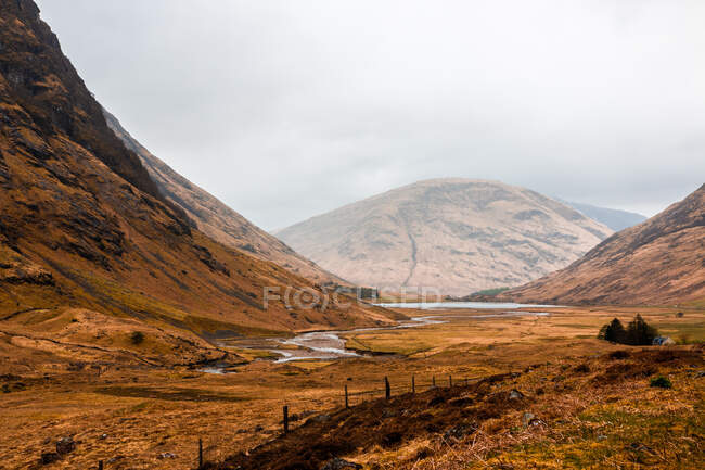 Narrow curvy road running through hilly terrain with dry grass among rocky mountains in cloudy spring day in Scottish Highlands — Stock Photo