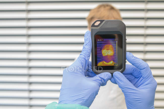 Unrecognizable medic in protective gloves and uniform using thermal imaging camera for checking temperature of kid on street during coronavirus outbreak — Stock Photo