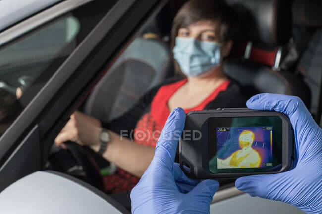 Crop doctor in medical gloves measuring temperature of female driver while using infrared camera during coronavirus epidemic — Stock Photo