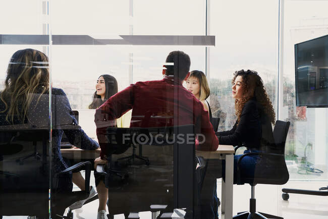Jóvenes colegas ocupados enfocados en ropa casual usando gadgets y tomando notas mientras trabajan juntos en la mesa en el espacio de coworking contemporáneo - foto de stock