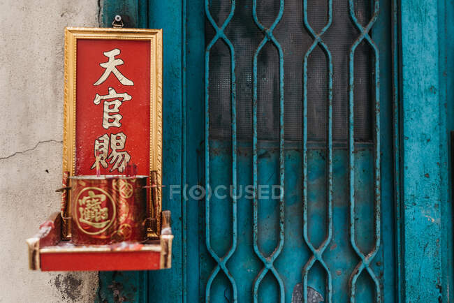 Exterior of metal door with picture of hieroglyphs with red small shrine hanging on wall of residential house in Hong Kong — Stock Photo