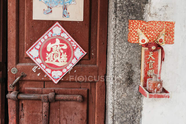 Exterior de puerta de madera con cuadro de jeroglífico con pequeño santuario rojo colgando en la pared de la casa residencial en Hong Kong - foto de stock