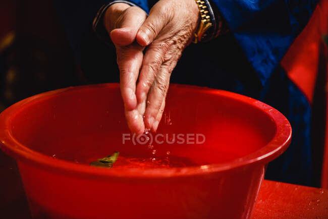 Gesichtslose religiöse Person legt Hände für rituelles Händewaschen in rote Schüssel — Stockfoto