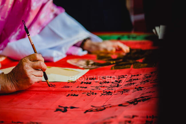 Crop master in kimono painting black hieroglyphs with ink on red textile in temple of Hong Kong — Stock Photo