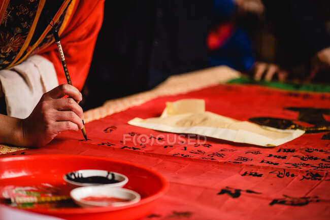 Erntemeister im Kimono bemalt schwarze Hieroglyphen mit Tinte auf rotem Textil im Tempel von Hongkong — Stockfoto