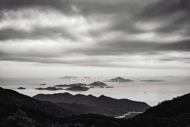 Picturesque view of shore with bay and misty mountains under cloudy sky in Hong Kong, black and white — Stock Photo