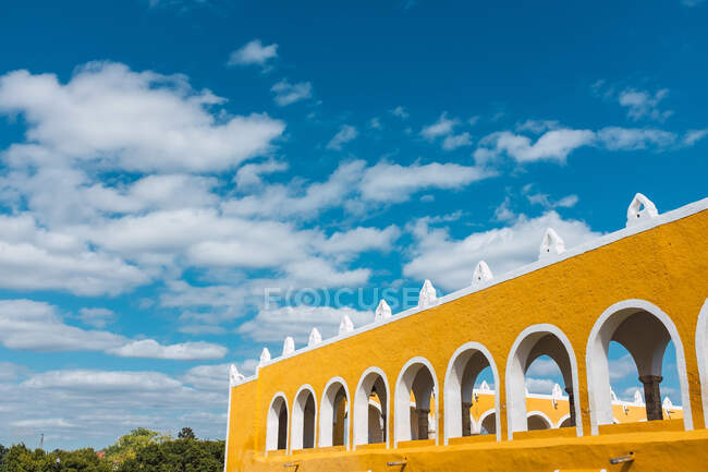 Exterior de paredes amarelas vivas com arcos na antiga cidade de Izamal contra o céu azul — Fotografia de Stock