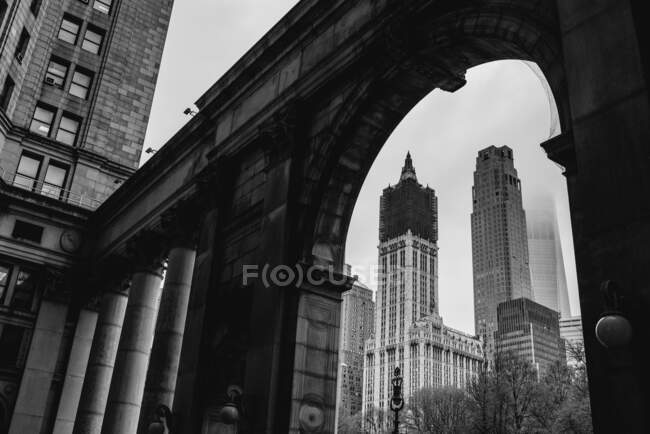 De baixo de paisagem urbana preta e branca de Woolworth Building sob reconstrução e pedra arqueada passagem com colunas em Manhattan — Fotografia de Stock