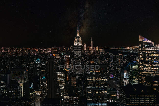 Veduta aerea di megalopoli con pareti di vetro illuminate e facciate futuristiche di alti skyline sullo sfondo la sera — Foto stock