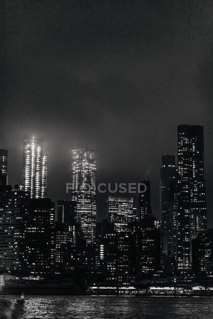 Complesso in bianco e nero di moderni skyline illuminati a Manhattan situato di fronte a un fiume calmo durante la notte — Foto stock