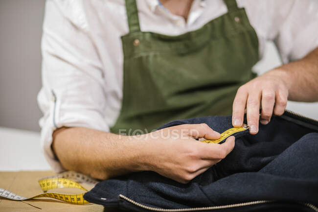 Unerkennbare männliche Näherin benutzt Maßband, während sie die exakte Größe der Muster überprüft, während sie maßgeschneiderte Outfits für den Kunden im modernen Atelier herstellt — Stockfoto