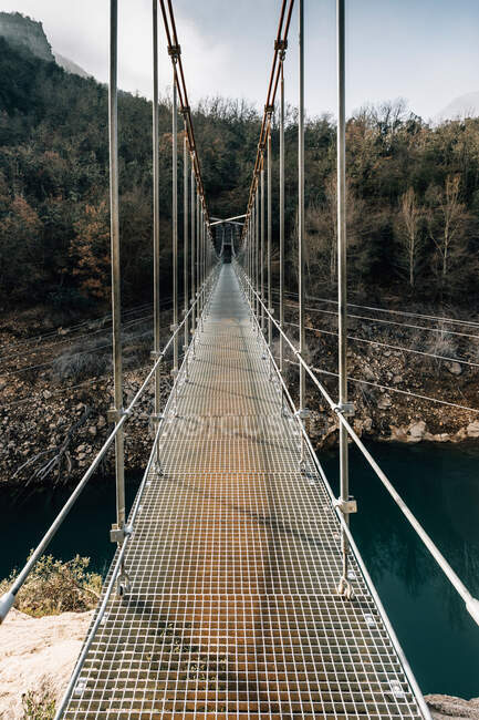 Пустой узкий пешеходный мост, подвешенный над рекой и соединяющий грубые породы хребта Монсек в Испании — стоковое фото