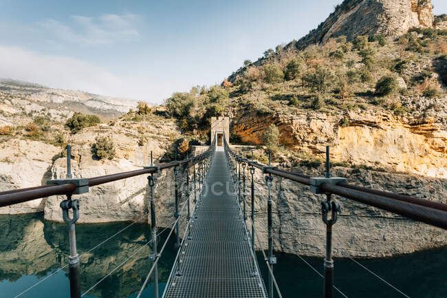 Пустой узкий пешеходный мост, подвешенный над рекой и соединяющий грубые породы хребта Монсек в Испании — стоковое фото