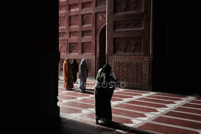 Visão traseira de mulheres irreconhecíveis vestindo hijab tradicional entrando na antiga mesquita com piso ornamental e paredes — Fotografia de Stock