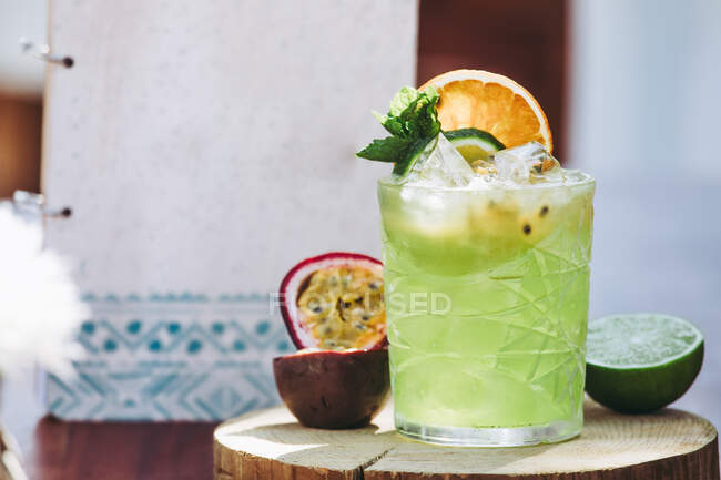 Copo de coquetel de álcool verde frio com maracujá fresco e limão decorado com folhas de hortelã e metades de frutas — Fotografia de Stock
