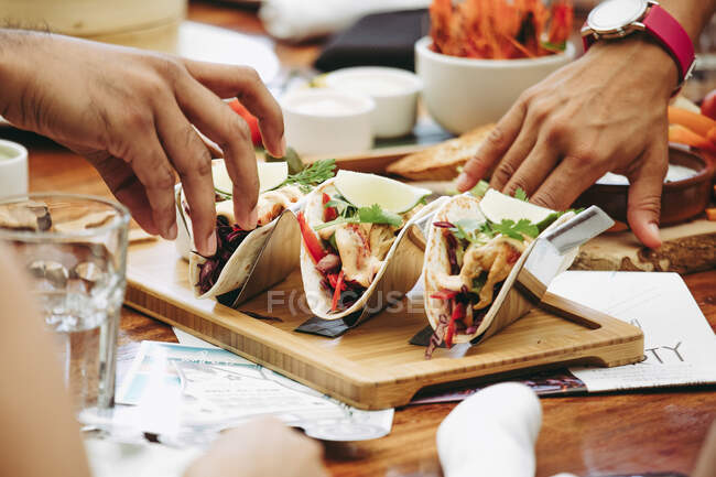 Mão atingindo tacos mexicanos tradicionais servidos em bandeja de madeira — Fotografia de Stock