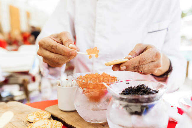 Crop unrecognizable person putting red caviar on small flatbread while standing at buffet table during party — Stock Photo