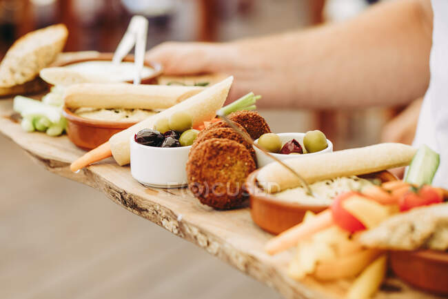 Cropped shot of person holding rustic wooden tray with various types of appetizers — Stock Photo