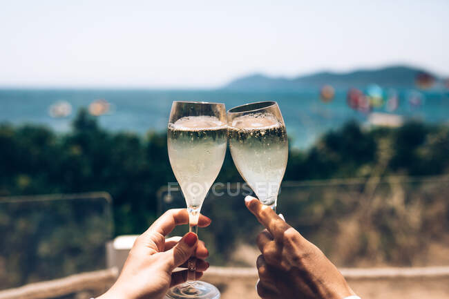 Mãos torcendo com copos de champanhe e paisagem ensolarada marinha no fundo — Fotografia de Stock